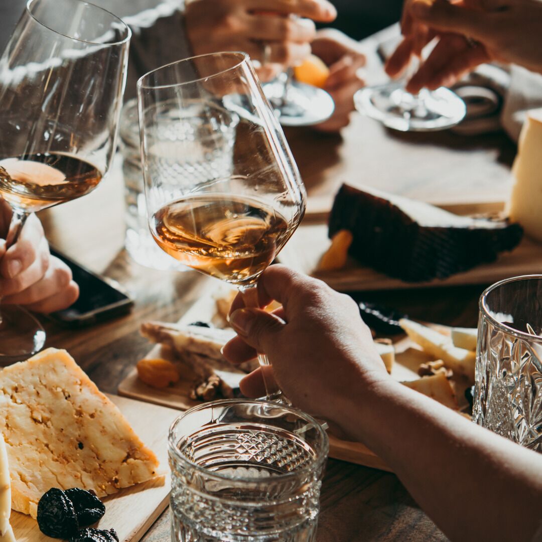 Un groupe de personnes trinquant avec des verres de vin autour d’une table où se trouvent du fromage et des crackers.