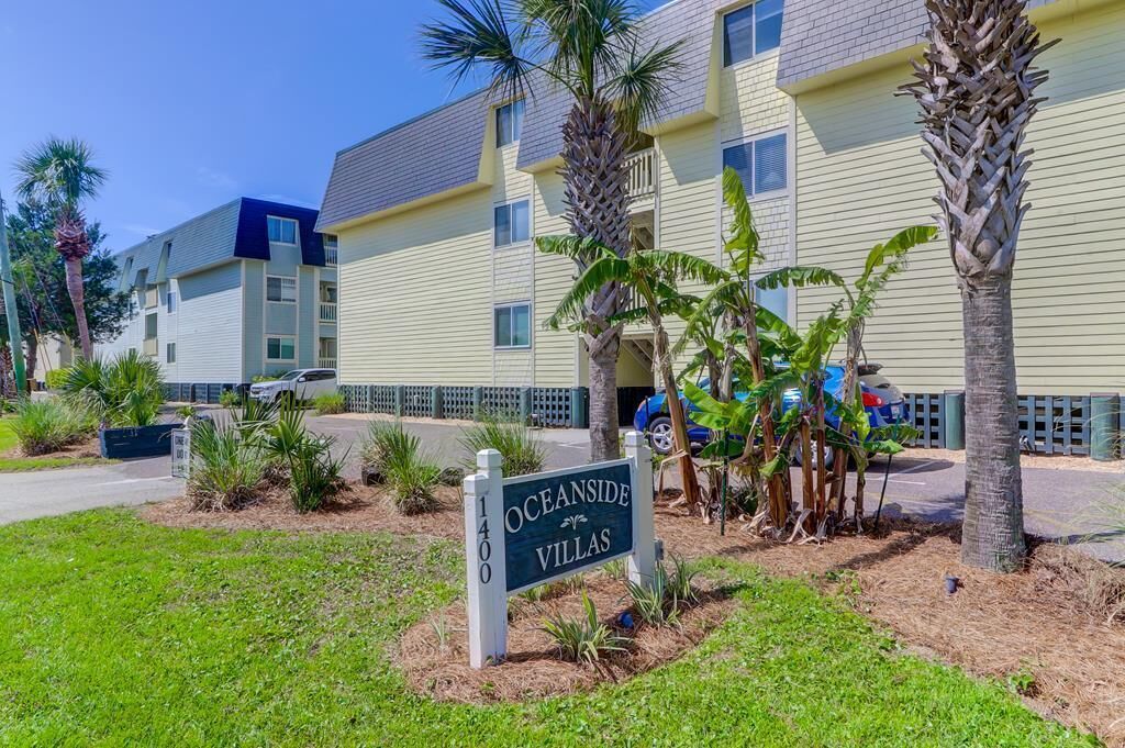 Señal de Oceanside Villas, un edificio de varios pisos con fachada amarillo claro, palmeras y cielo despejado.