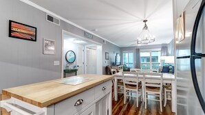A kitchen with a wooden countertop, white cabinets, and a dining area with white chairs and a table. - Modern Condo, Pool, Close to Beach, Restaurants & Shops - 101A Oceanside (Isle Of Palms)