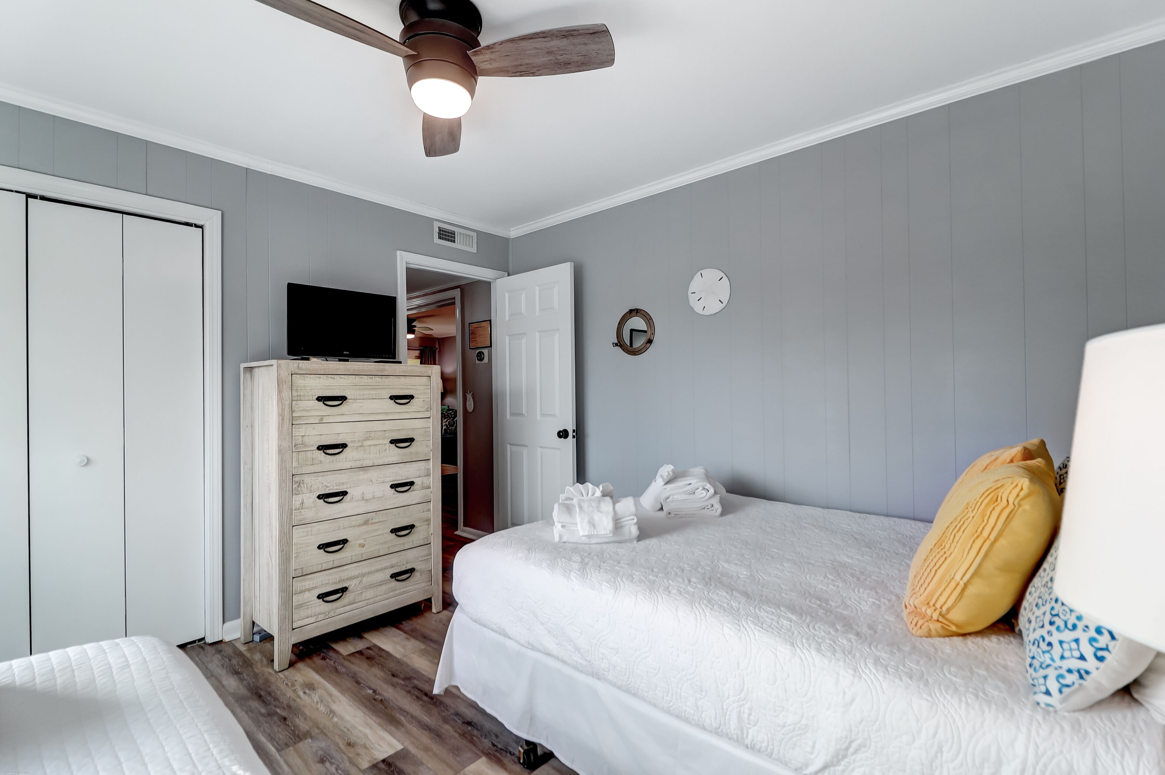 A bedroom with a bed, a dresser, a ceiling fan, and a door leading to another room.