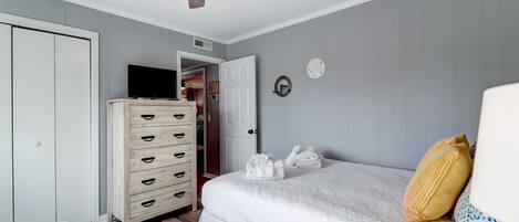 A bedroom with a bed, a dresser, a ceiling fan, and a door leading to another room.