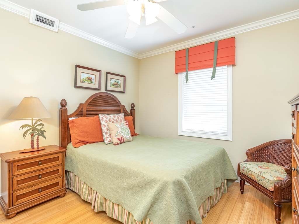 Un dormitorio con cama, mesita de noche, silla, ventana con persianas y ventilador de techo.