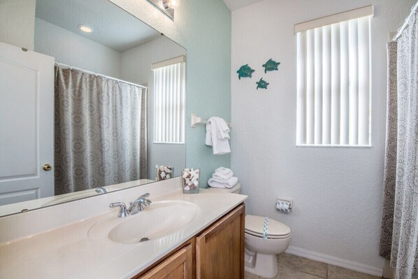 A bathroom with a sink, mirror, toilet, and decorative fish wall art. - 5 bed with spa on golf course community (Davenport)