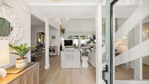 A spacious living area with a sofa, coffee table, and a TV. There is a wooden cabinet with a plant on it. The room has a large mirror and a door leading to another room. - Beautiful Renovation~Golf Course View~Golf Cart,Free Activities, Fenced Patio (Miramar Beach)