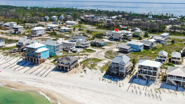 Vue aérienne d’un quartier résidentiel situé sur la côte, avec des maisons, dont certaines donnent directement sur la plage, et une vue dégagée sur l’océan.