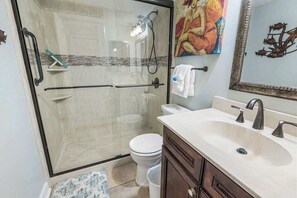 Une salle de bain avec une douche à parois de verre, des toilettes, un lavabo avec un miroir et un tableau au mur.