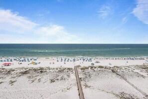 Une plage avec une promenade en bois menant à l’eau, des rangées de parasols et un ciel dégagé.