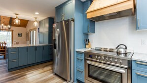 A modern kitchen with blue cabinets, stainless steel appliances, and a wooden ceiling.