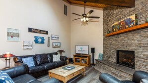 A cozy living room with a stone fireplace, leather sofas, a wooden coffee table, and various wall decorations.