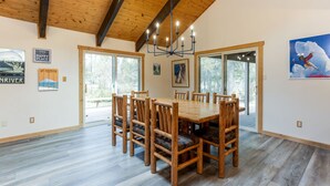 A dining area with a wooden table and chairs, large windows, and a chandelier.