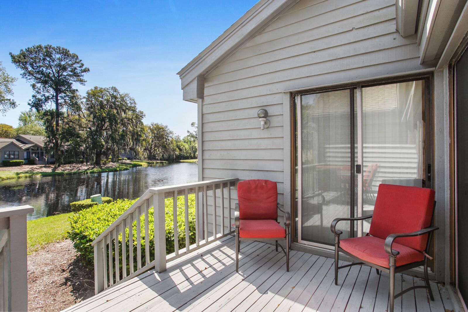 A wooden deck with two red chairs and a glass door leading to a covered area.