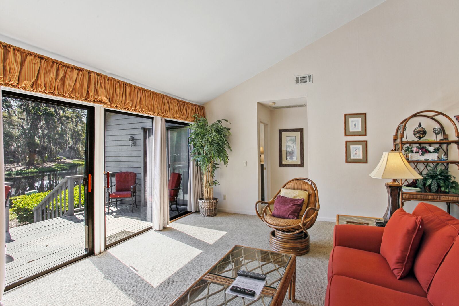 Sala de estar com sofá vermelho, cadeira de vime, mesa de centro de vidro e uma janela grande com vista para um deck.
