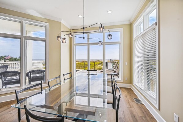 Enjoy meals in this dining area with a large table and comfortable chairs, surrounded by large windows offering a view of the outdoors.