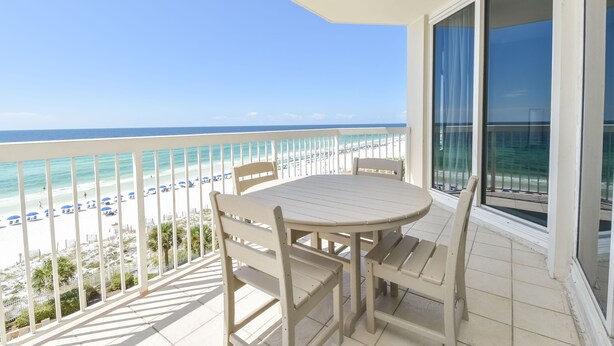 Varanda com mesa e cadeiras com vista para uma praia com guarda-sóis.
