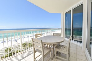 A balcony with a table and chairs overlooking a beach with umbrellas.