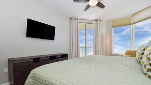 Quarto com uma cama grande, televisão de tela plana na parede, cómoda de madeira escura e janela com cortinas.
