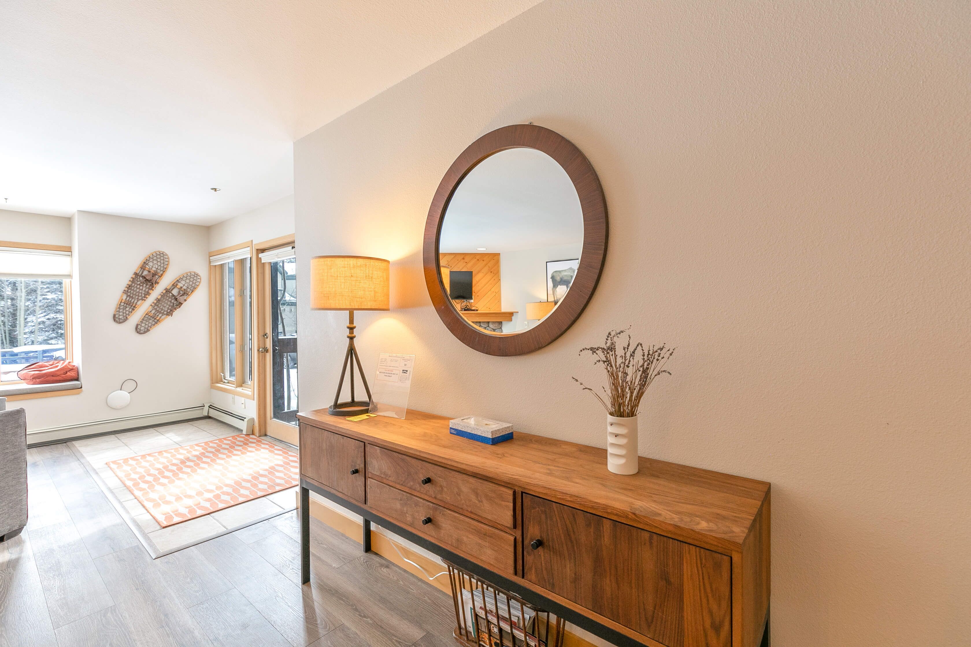 A modern entryway with a wooden console, a round mirror, and a vase with dried plants.