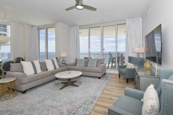 A spacious living room with a large sectional sofa, a round coffee table, and a view of the ocean through large sliding doors. - Upscale crisp, coastal beachfront condo w/private balcony! (Destin)