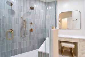 A modern bathroom with a glass shower enclosure, a white vanity with gold fixtures, and a large mirror. - Upscale crisp, coastal beachfront condo w/private balcony! (Destin)