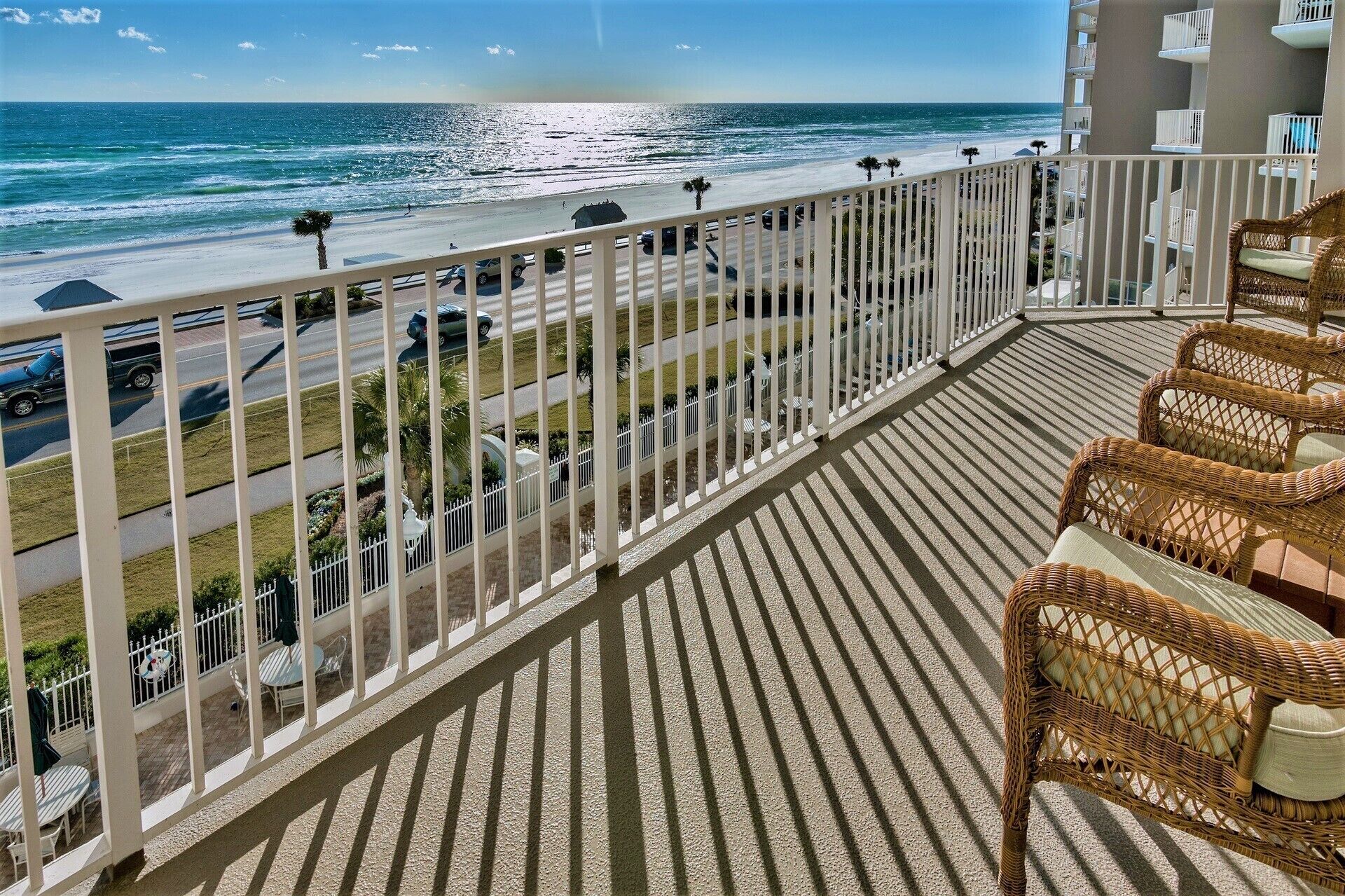 Ein Balkon mit Korbstühlen, Blick auf den Strand und ein Parkplatz.