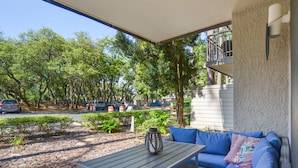 Une terrasse extérieure avec une table et un canapé bleu, entourée d’arbres et offrant une vue sur les voitures garées.