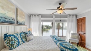 A bedroom with a large bed, a ceiling fan, and a view of a lake through the window. - Renovated Beach Villa w/GOLF CART, Lakeside, Beach, Pool/Hot Tub, Tram, Grill (Miramar Beach)