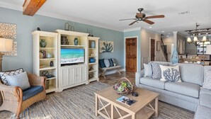 A living room with a television, wicker furniture, a grey sofa, and a ceiling fan. - Renovated Beach Villa w/GOLF CART, Lakeside, Beach, Pool/Hot Tub, Tram, Grill (Miramar Beach)