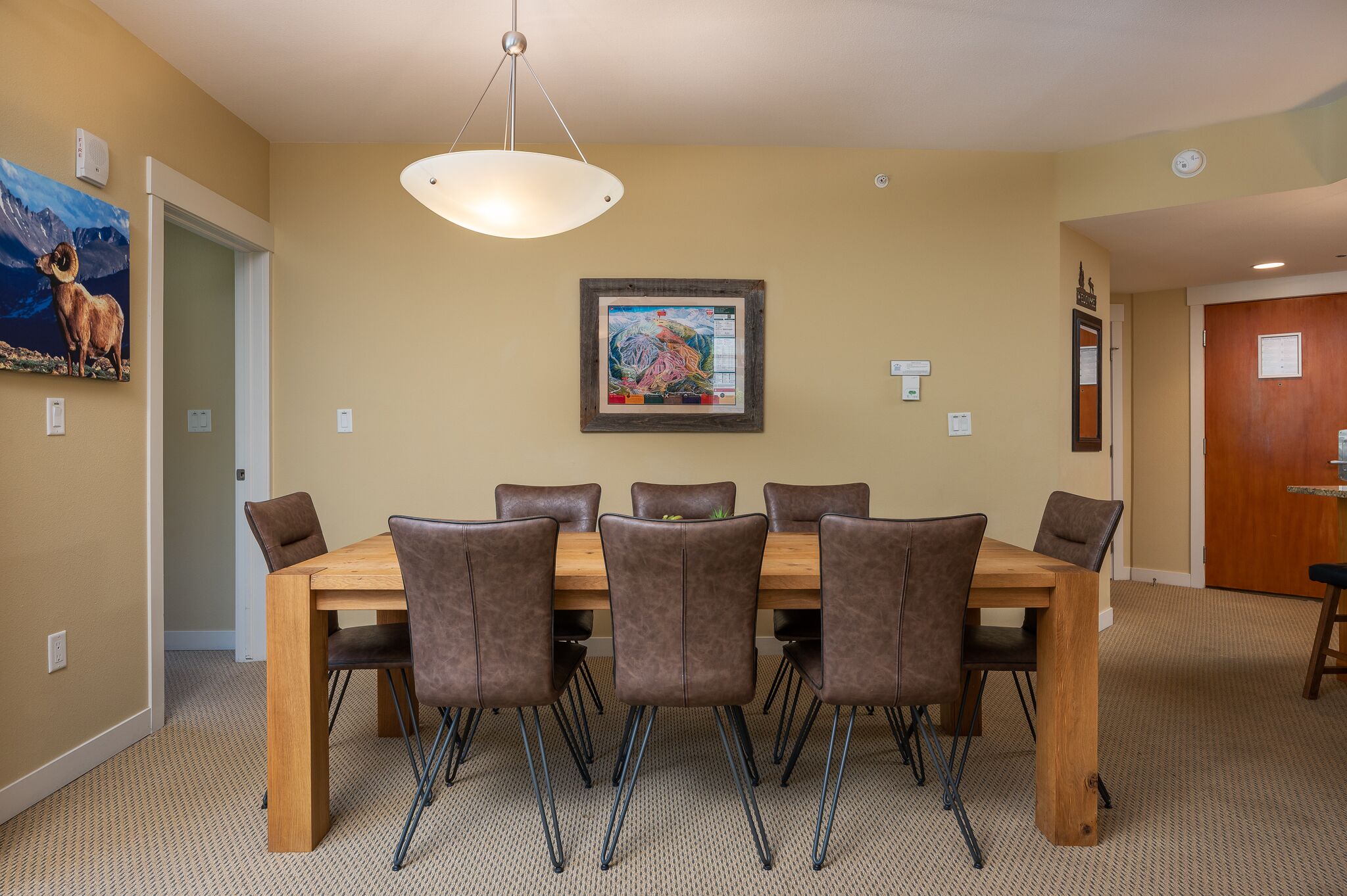 A dining area with a wooden table and six chairs, a hanging light fixture, and a framed picture on the wall.