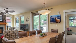 Uma sala de estar espaçosa com uma grande mesa de jantar de madeira, assentos confortáveis, lareira e uma janela ampla com vista para o exterior.
