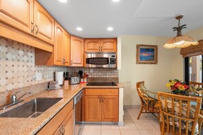 Una cocina con armarios de madera, un microondas de acero inoxidable, un fregadero y una zona de comedor con una mesa y sillas.