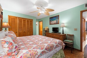 A bedroom with a bed, a ceiling fan, a television, a wooden wardrobe, and a chair. - Island Charm: Kihei Beach #305, Beachfront Condo Offers Spectacular Ocean Views! (Kihei, Maui)