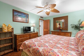A bedroom with a bed, a television, a ceiling fan, a painting, and a mirror.