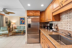 A kitchen with wooden cabinets, a stainless steel refrigerator, a granite countertop, and a sink.