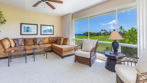 A living room with a sectional sofa, a wicker chair, a floor lamp, and a ceiling fan. - Emmalani Court #225 Fabulous Views!  Air Conditioning in Both Bedrooms (Princeville)