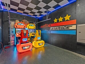 Une salle d’arcade proposant des jeux de course avec plusieurs simulateurs de course et un grand mur décoré d’une fresque sur laquelle on peut lire le texte « LETSRACE ».