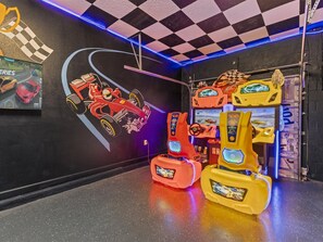 Une salle d’arcade sur le thème des courses automobiles, avec un sol à motifs en damier, des fresques représentant des voitures de course et des machines d’arcade aux couleurs vives.