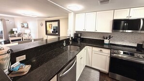 Una cocina moderna con armarios blancos, encimera negra, electrodomésticos de acero inoxidable y un comedor con vistas.