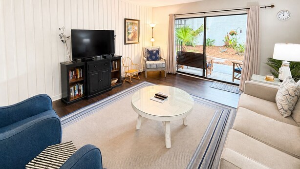 Una sala de estar con una televisión de pantalla plana, un sofá, una mesa de centro y un ventanal corredizo que da a un área exterior.