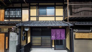 Un bâtiment japonais traditionnel, avec un toit recouvert de tuiles, une porte d’entrée en bois et une bannière violette suspendue.