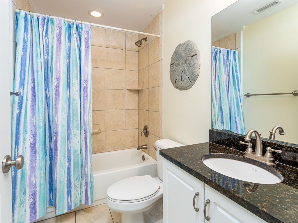 Une salle de bain équipée d’un rideau de douche, d’une baignoire, de toilettes, d’un lavabo et d’un élément décoratif mural.