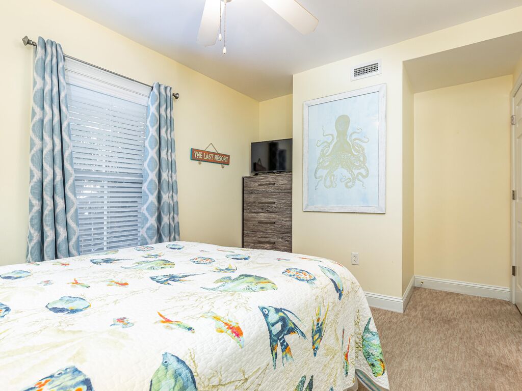 A bedroom with a bed, a television, a sign reading "The Land's End," and a framed octopus artwork on the wall.