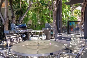 Eine Terrasse im Freien mit einem runden Tisch, Metallstühlen, einem Grill und einem Barbecue.