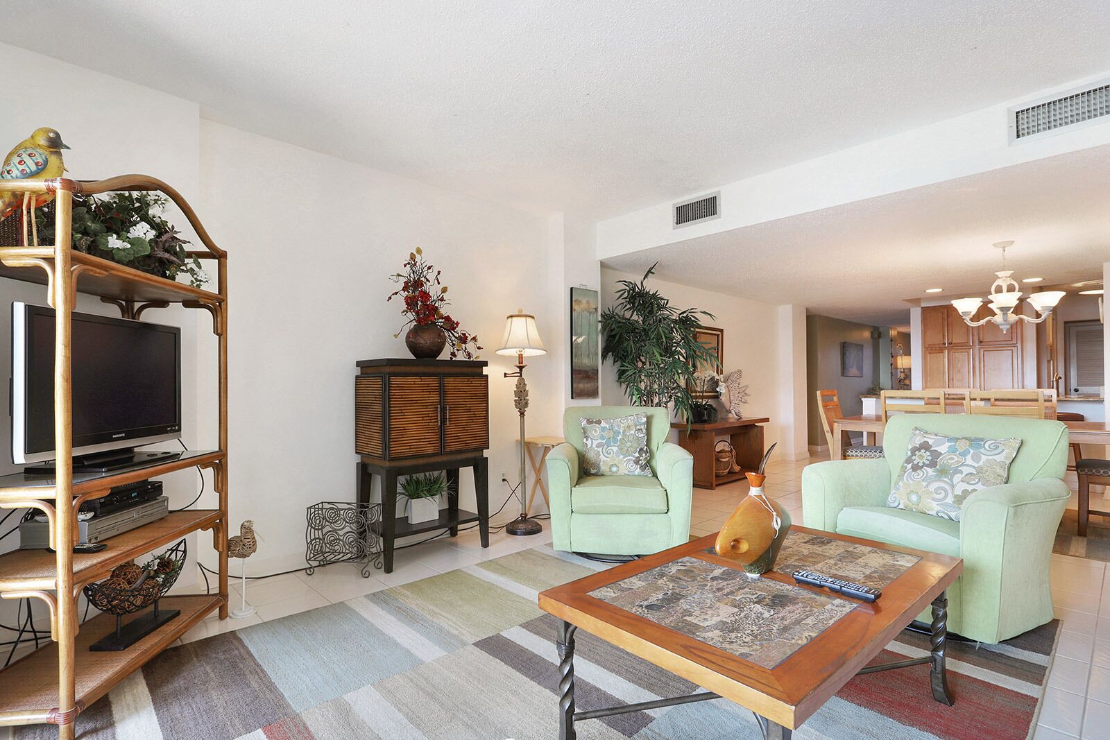 A living room with a television, a wooden entertainment unit, a sofa, a coffee table, and a dining area in the background.
