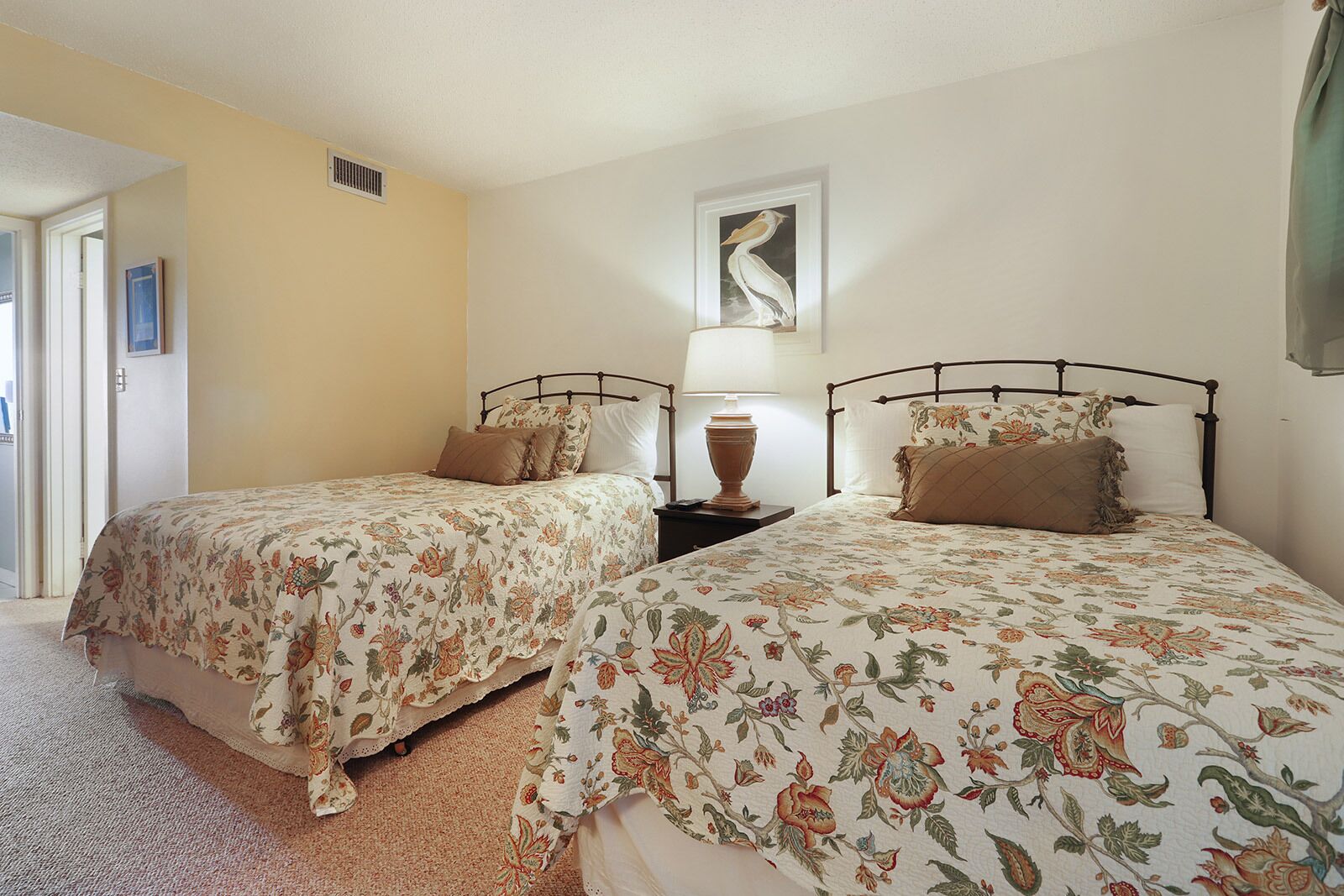 A bedroom with two beds, each with floral bedding, a bedside table with a lamp, and a wall-mounted artwork.