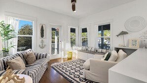 A spacious living room with a large window, a sofa, a coffee table, and a patterned rug. - Seagrove Beach Home + Carriage House + Bikes (Santa Rosa Beach)