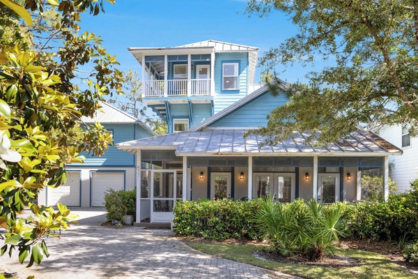 Charming coastal home with distinctive blue siding and metal roof, featuring wraparound porches and mature landscaping in a peaceful setting.