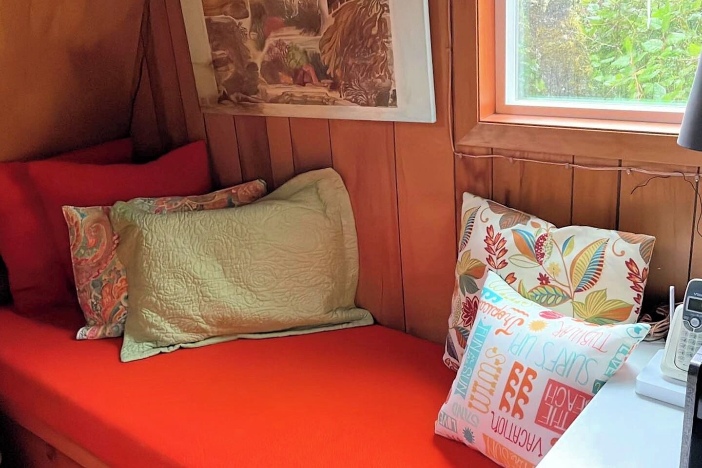 Una habitación acogedora con pared de madera, colcha roja y ventana con vista a vegetación.