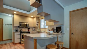 A modern kitchen with a central island, wooden stools, and built-in appliances.