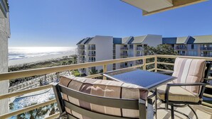 A balcony with a table and chairs, overlooking a beach and a row of buildings.