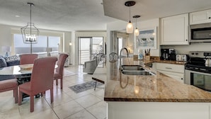 A modern kitchen with a large island, stainless steel appliances, and a view to the ocean.